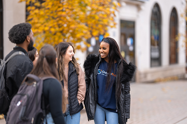 Students talking on the sidewalk with a fall tree in the background