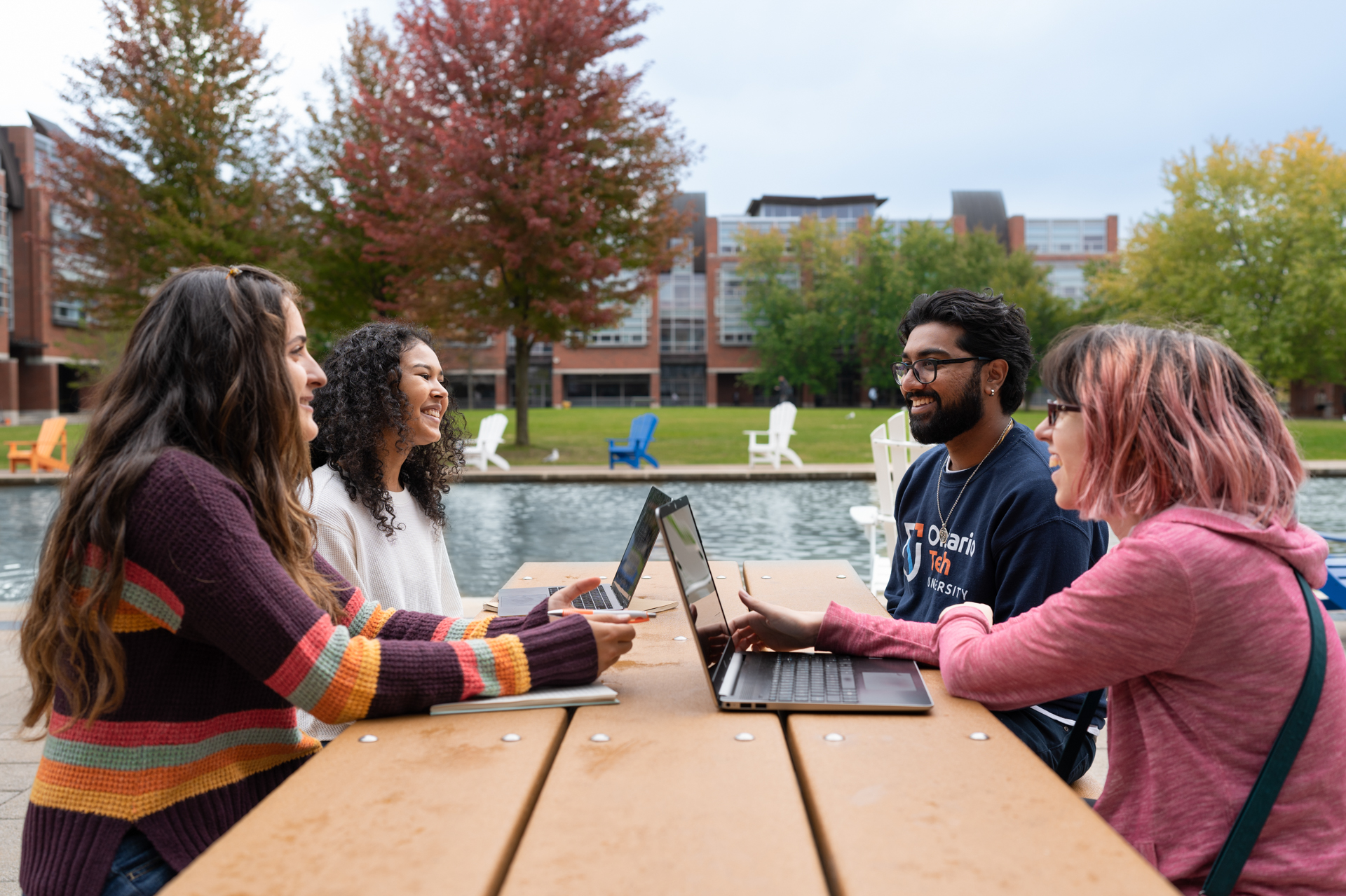 Four students sitting at a picnic table by a pond
